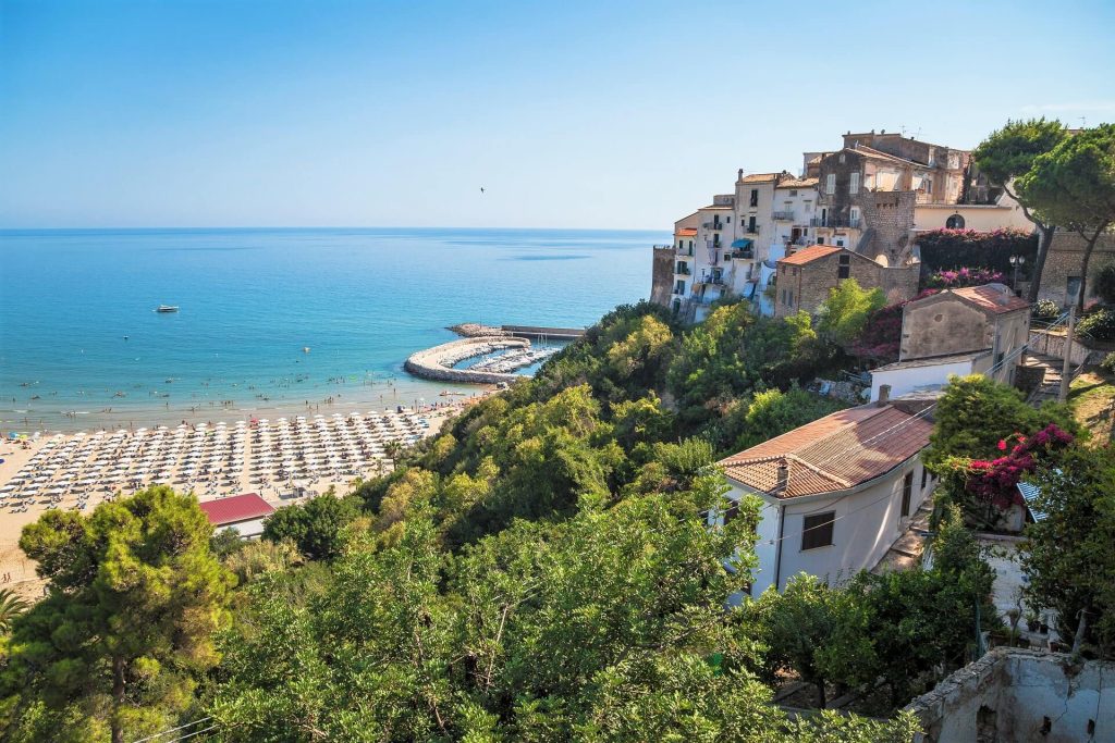 Scorcio di una città costiera con spiaggia, mare blu e case arroccate sulla collina.